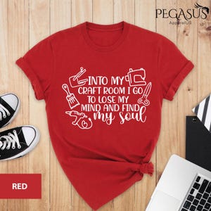 K&ouml;nnte beinhalten: Rotes T-Shirt mit wei&szlig;em Text, der lautet "Into my craft room I go to lose my mind and find my soul". Der Text ist von verschiedenen Bastelwerkzeugen umgeben, darunter ein Pinsel, eine Schere, eine N&auml;hmaschine und eine Bohrmaschine.