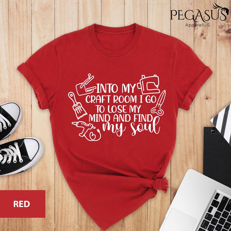 K&ouml;nnte beinhalten: Rotes T-Shirt mit wei&szlig;em Text, der lautet "Into my craft room I go to lose my mind and find my soul". Der Text ist von verschiedenen Bastelwerkzeugen umgeben, darunter ein Pinsel, eine Schere, eine N&auml;hmaschine und eine Bohrmaschine.