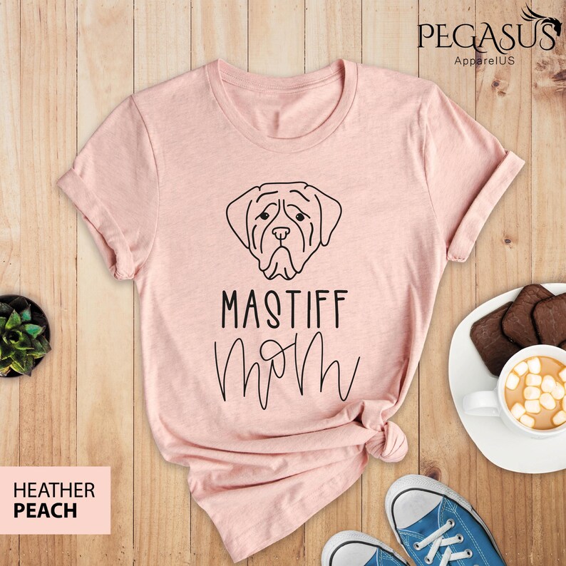 K&ouml;nnte beinhalten: Ein rosa T-Shirt mit einer schwarzen Linienzeichnung eines Mastiff-Hundekopfes und dem Text "Mastiff Mom" in einer kursivschriftlichen Schrift.