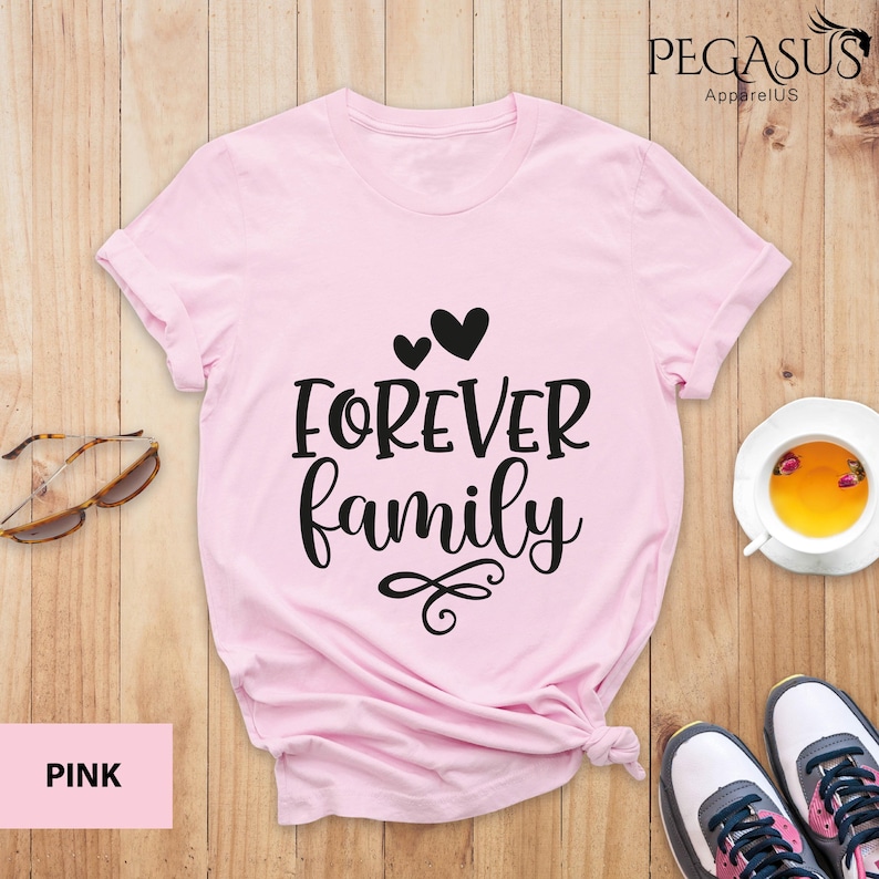 Pode incluir: Camiseta rosa com o texto "FOREVER family" em letras pretas e dois pequenos cora&ccedil;&otilde;es acima do texto.