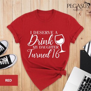 May include: Red t-shirt with white text that reads "I deserve a drink my daughter turned 16" and a white wine glass graphic.