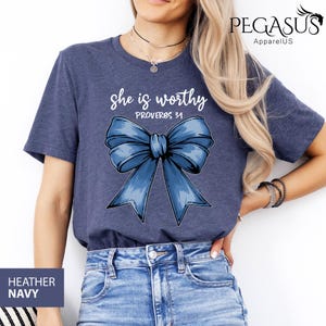 May include: A heather navy blue t-shirt with a blue bow and the text "She is worthy Proverbs 31" printed on the front.