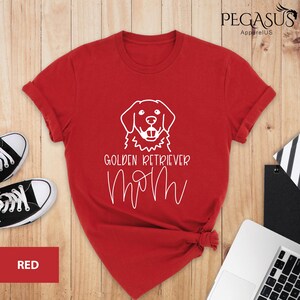 Op de afbeelding: Rood T-shirt met een witte omtrek van een golden retriever en de tekst "Golden Retriever Mom".