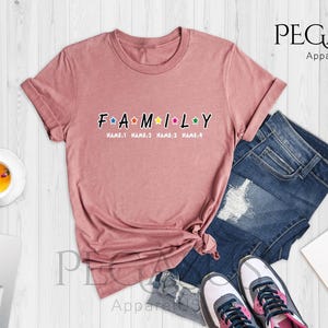 May include: Heather mauve t-shirt with the word "FAMILY" in rainbow letters with stars in between each letter. The text "NAME 1 NAME 2 NAME 3 NAME 4" is below the word "FAMILY".