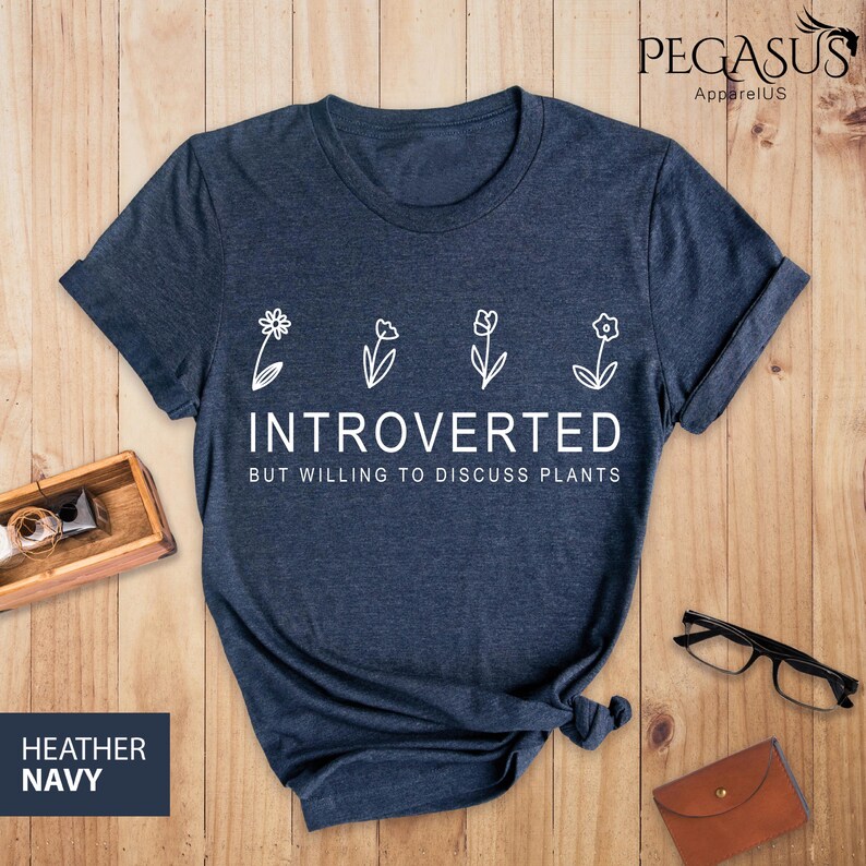 May include: A heather navy blue t-shirt with a white graphic of four flowers and the text "Introverted but willing to discuss plants".
