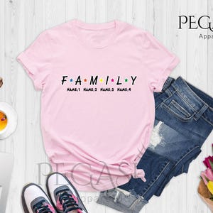 May include: Pink t-shirt with the word "FAMILY" in black letters with colorful stars between each letter. The text "NAME 1 NAME 2 NAME 3 NAME 4" is printed below the word "FAMILY".