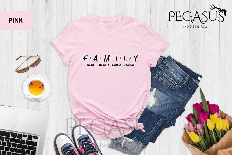May include: Pink t-shirt with the word "FAMILY" in black letters with colorful stars between each letter. The text "NAME 1 NAME 2 NAME 3 NAME 4" is printed below the word "FAMILY".