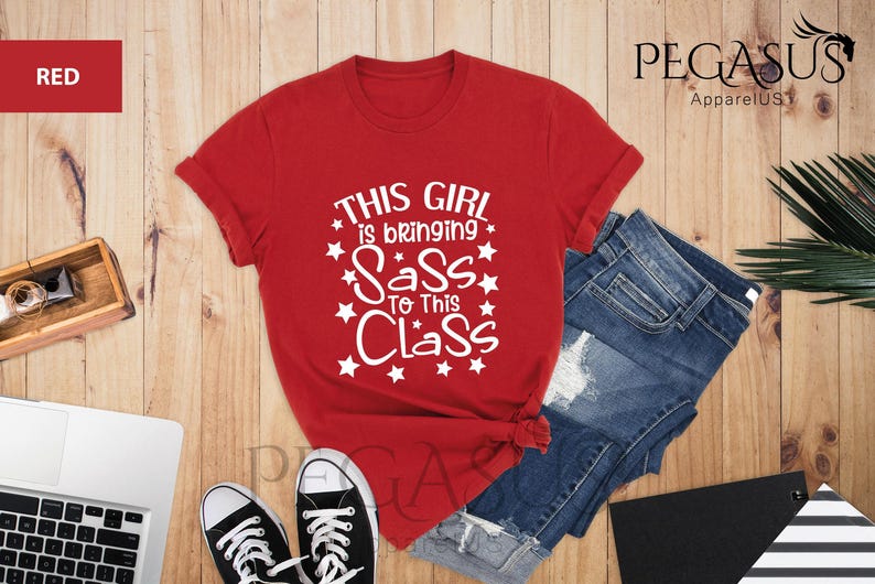 K&ouml;nnte beinhalten: Rotes T-Shirt mit wei&szlig;em Text, der "This girl is bringing sass to this class" lautet, umgeben von wei&szlig;en Sternen.