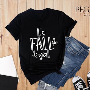 Può includere: Maglietta nera con testo bianco che dice "It's Fall y'all".