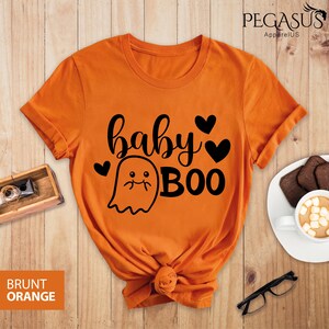 May include: Burnt orange t-shirt with the text "baby BOO" in black script and a ghost graphic. The shirt has a round neck and short sleeves. The brand name "PEGASUS ApparelUS" is printed at the top.