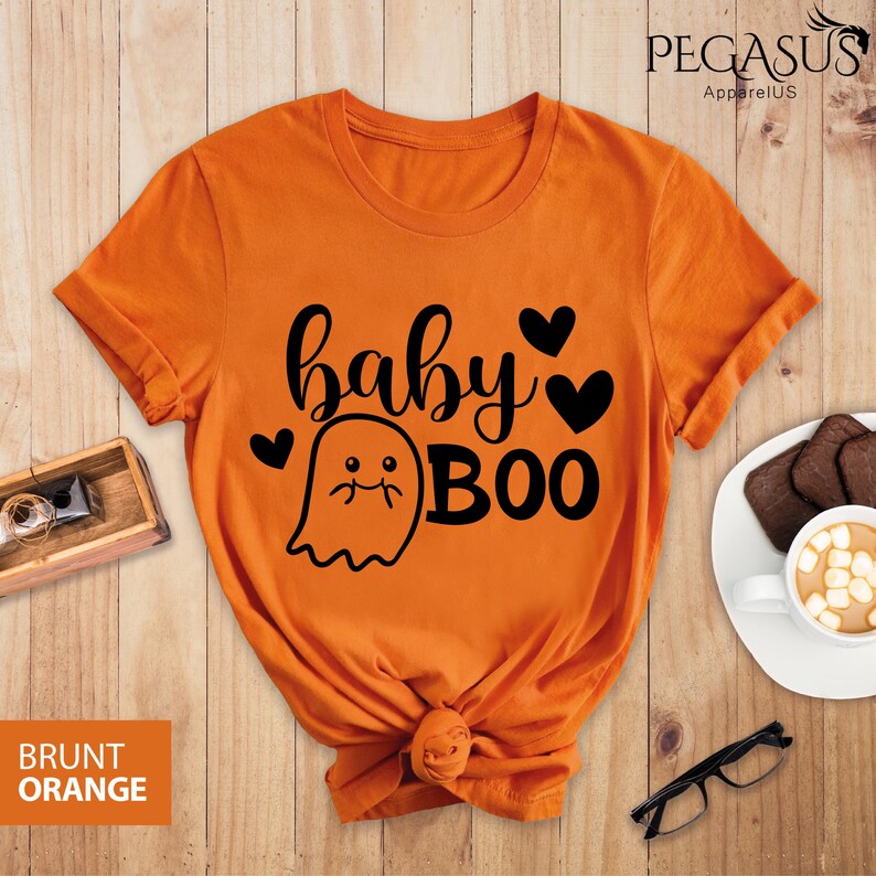 May include: Burnt orange t-shirt with the text "baby BOO" in black script and a ghost graphic. The shirt has a round neck and short sleeves. The brand name "PEGASUS ApparelUS" is printed at the top.