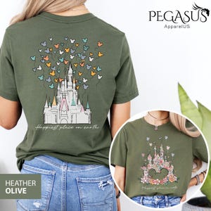 Op de afbeelding: Een groen T-shirt met een afbeelding van Assepoester's kasteel en de tekst "Happiest place on earth". Het kasteel is omringd door kleurrijke Mickey Mouse ballonnen.