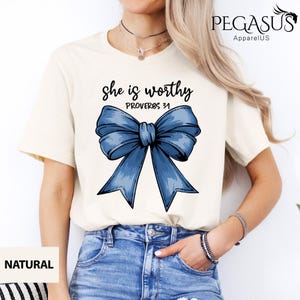 May include: A white t-shirt with a blue bow and the text "She is worthy Proverbs 31" printed on it.