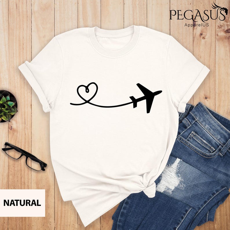 Puede incluir: Camiseta blanca con un avi&oacute;n y un coraz&oacute;n negros. El avi&oacute;n vuela lejos de un coraz&oacute;n que est&aacute; dibujado con una l&iacute;nea.