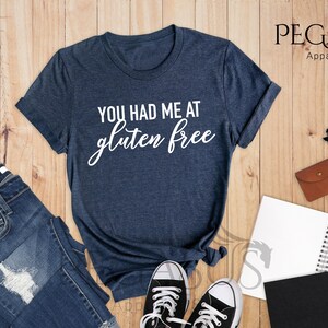 K&ouml;nnte beinhalten: Ein T-Shirt in Marineblau mit dem Aufdruck "You had me at gluten free" in Wei&szlig; auf der Vorderseite.