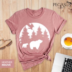Puede incluir: Camiseta de color malva jaspeado con un gr&aacute;fico blanco de un oso y un cachorro en una escena de bosque con un p&aacute;jaro volando por encima. El gr&aacute;fico est&aacute; dentro de un c&iacute;rculo con una forma de luna blanca.