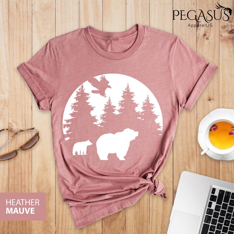 Puede incluir: Camiseta de color malva jaspeado con un gr&aacute;fico blanco de un oso y un cachorro en una escena de bosque con un p&aacute;jaro volando por encima. El gr&aacute;fico est&aacute; dentro de un c&iacute;rculo con una forma de luna blanca.
