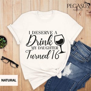 May include: White t-shirt with black text that reads "I deserve a drink my daughter turned 16" with a wine glass graphic.