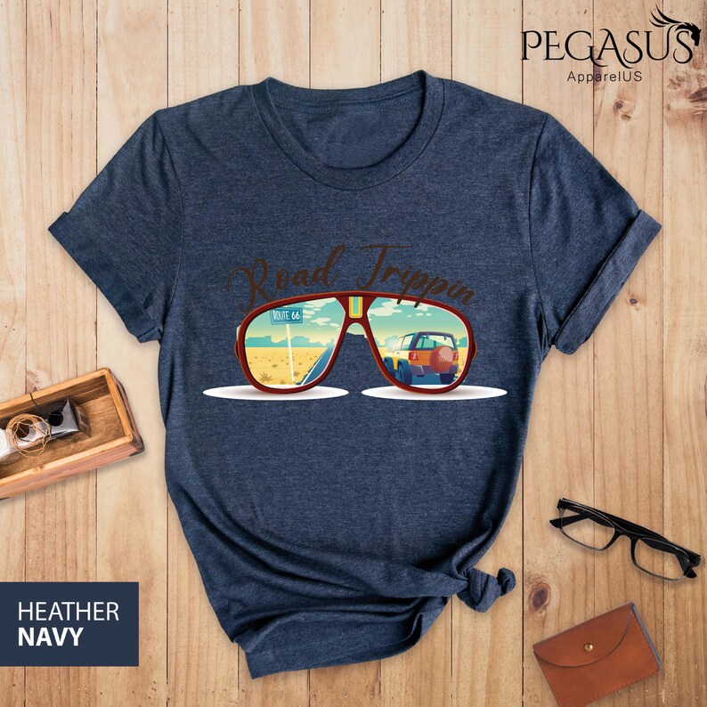 Peut inclure: Un t-shirt bleu marine chin&eacute; avec un graphique de lunettes de soleil refl&eacute;tant une sc&egrave;ne de road trip. Le texte "Road Trippin'" est au-dessus des lunettes de soleil.