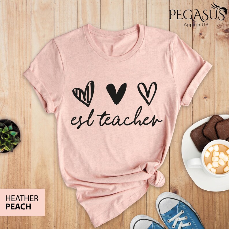 May include: A pink t-shirt with three black hearts and the text "esl teacher" printed on the front.