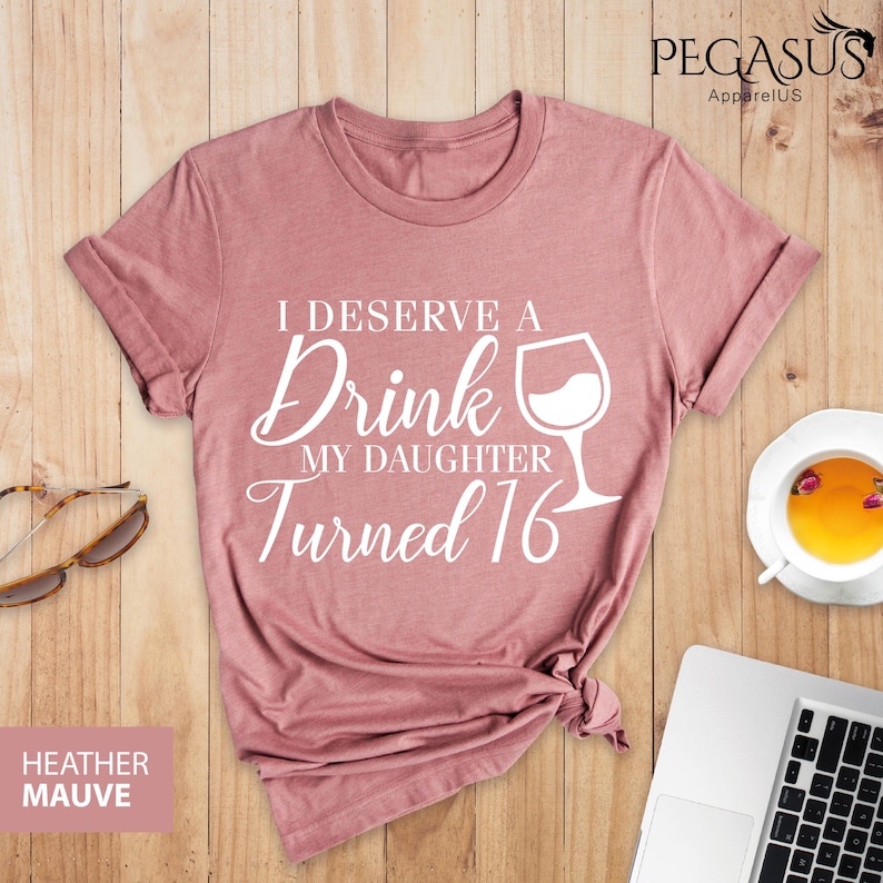 May include: A heather mauve t-shirt with the text "I deserve a drink my daughter turned 16" and a wine glass graphic.