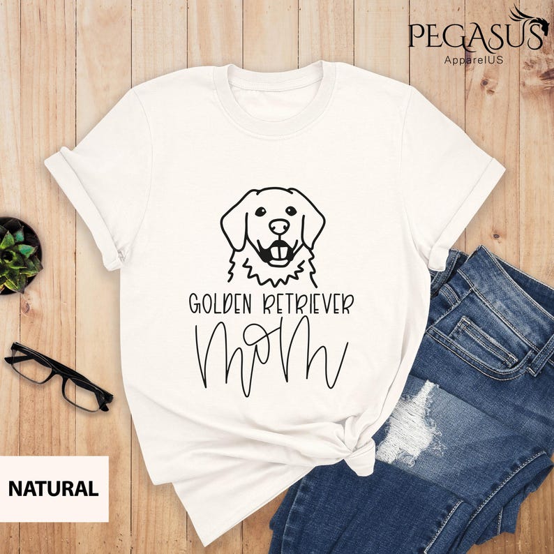 Op de afbeelding: Wit T-shirt met een zwarte omtrek van een golden retriever hond en de tekst "Golden Retriever Mom" in zwart.