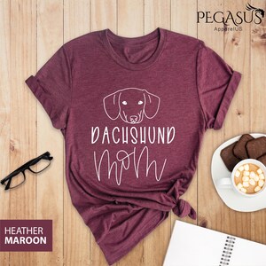 May include: Heather maroon t-shirt with a white outline of a dachshund and the text "Dachshund Mom" in white.