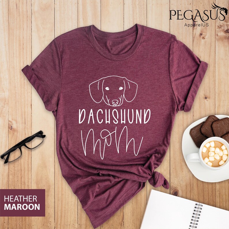 May include: Heather maroon t-shirt with a white outline of a dachshund and the text "Dachshund Mom" in white.
