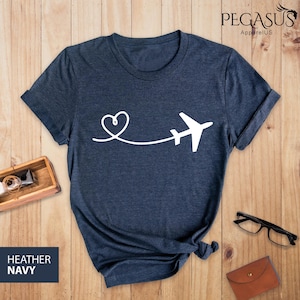 Puede incluir: Una camiseta azul marino jaspeada con un avi&oacute;n y un coraz&oacute;n blancos. El avi&oacute;n est&aacute; volando lejos de un coraz&oacute;n.