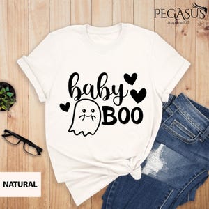 May include: White t-shirt with the text "baby BOO" in black script and a cute ghost graphic. The design includes black hearts. The shirt is paired with blue jeans.
