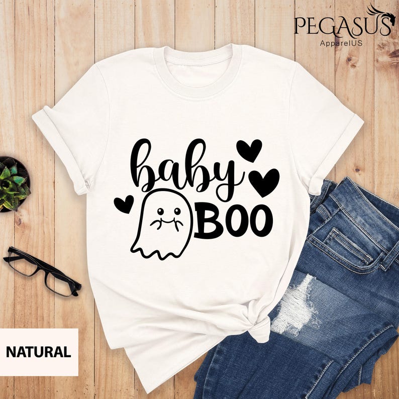 May include: White t-shirt with the text "baby BOO" in black script and a cute ghost graphic. The design includes black hearts. The shirt is paired with blue jeans.