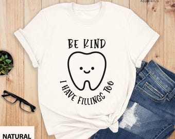 May include: White t-shirt with a black graphic of a smiling tooth and the text "Be Kind I Have Fillings Too".