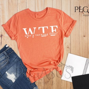 May include: Heather orange t-shirt with the text "WTF who's turning fifty?" printed in white.