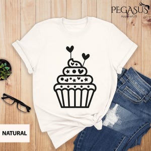 May include: White t-shirt with a black cupcake graphic. The cupcake has hearts and stars on it.