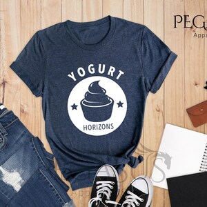 May include: A heather navy blue t-shirt with a white circle graphic that says "Yogurt Horizons" and features a stylized image of a yogurt cup with a swirl of yogurt on top.