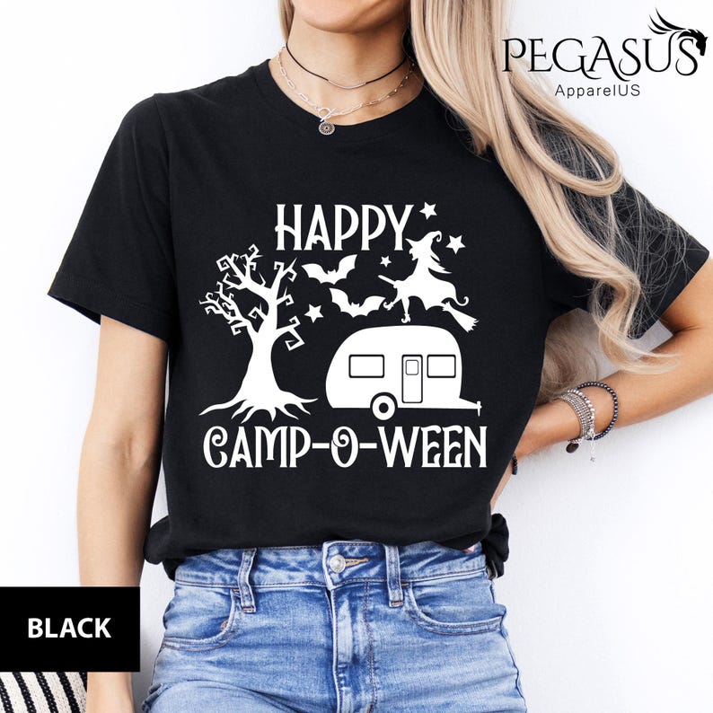 May include: Black t-shirt featuring a white graphic with the text "HAPPY CAMP-O-WEEN". The design includes a tree, bats, a witch on a broom, and a caravan. The shirt has a crew neck and short sleeves.