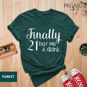 May include: A dark green t-shirt with the text "Finally 21 buy me a drink" in white.