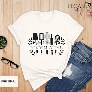 May include: White t-shirt with a black graphic of kitchen utensils and the text "CUSTOM NAME" in a decorative font.