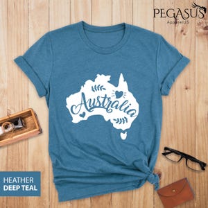 Op de afbeelding: Een heide-diepblauw t-shirt met een witte omtrek van het continent Australi&euml; en het woord "Australi&euml;" in een gestileerd lettertype. Een klein hartje bevindt zich binnen de omtrek van het continent.