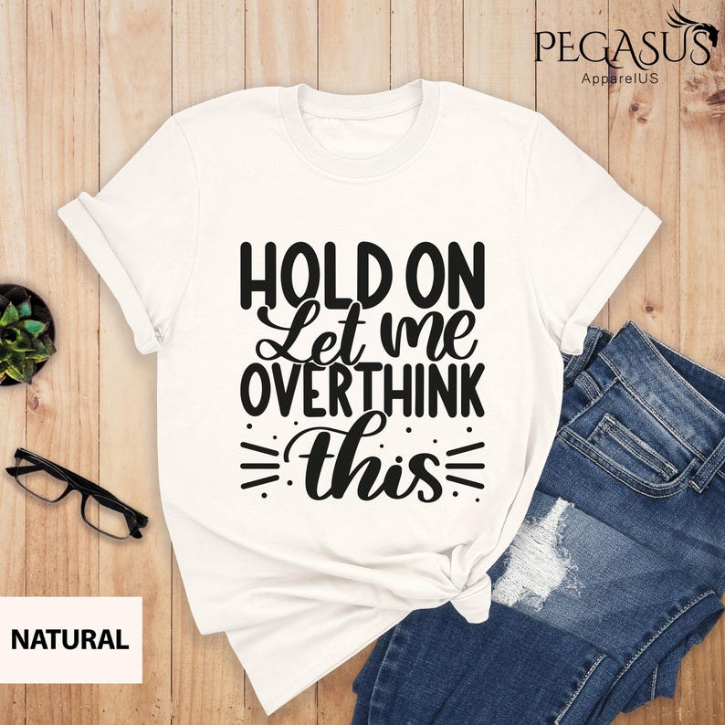 May include: White t-shirt with black text that reads "Hold on Let me overthink this".