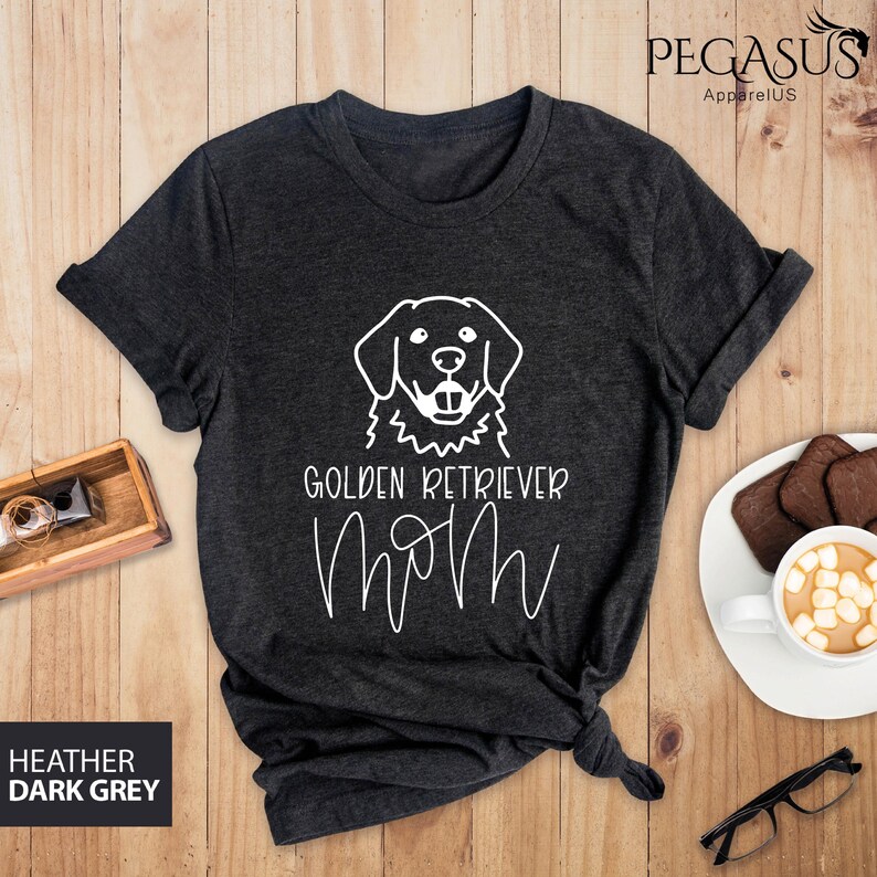 Op de afbeelding: Heather donkergrijs T-shirt met een witte omtrek van een golden retriever en de tekst "Golden Retriever Mom" in wit.