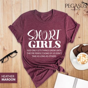 May include: Heather maroon t-shirt with the text "SHORT GIRLS" in white. The text below reads "GOD ONLY LETS THINGS GROW UNTIL THEY'RE PERFECT; SOME OF US DON'T TAKE AS LONG AS OTHERS".