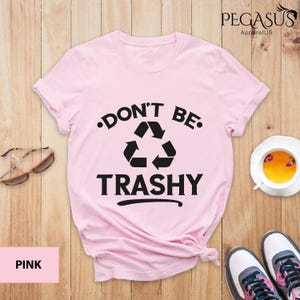 May include: Pink t-shirt with a black graphic that says "Don't Be Trashy" with a recycling symbol.