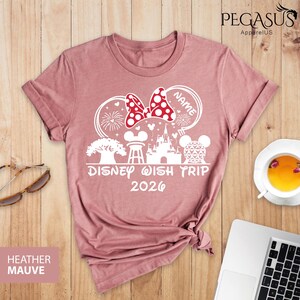 May include: Heather mauve t-shirt with a white graphic design featuring a Minnie Mouse bow with polka dots, fireworks, and the text "Disney Wish Trip 2026". The shirt also has a Mickey Mouse head and a castle.