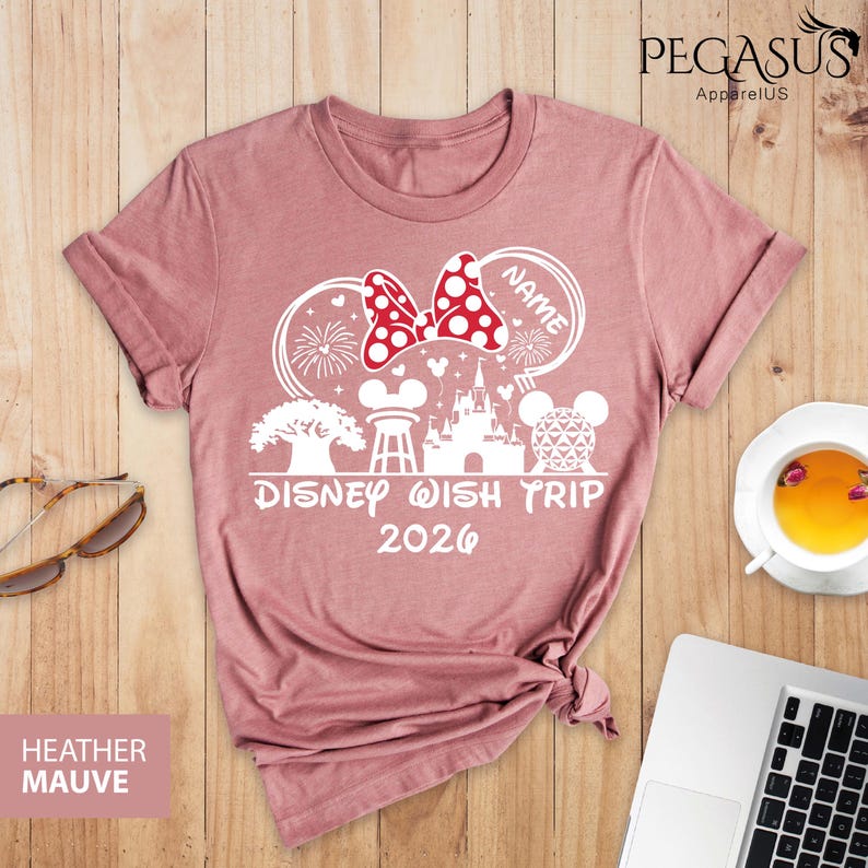 May include: Heather mauve t-shirt with a white graphic design featuring a Minnie Mouse bow with polka dots, fireworks, and the text "Disney Wish Trip 2026". The shirt also has a Mickey Mouse head and a castle.