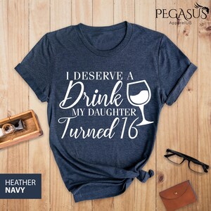 May include: A dark blue t-shirt with white text that reads "I deserve a drink my daughter turned 16" with a wine glass graphic.