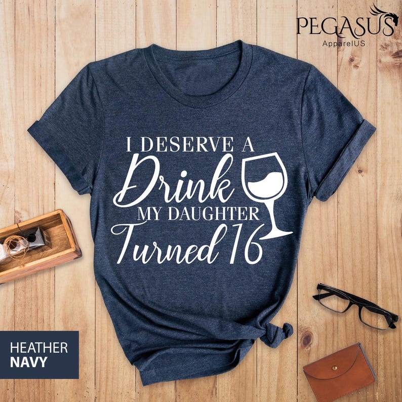 May include: A dark blue t-shirt with white text that reads "I deserve a drink my daughter turned 16" with a wine glass graphic.