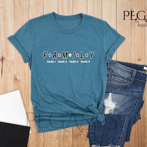 May include: A teal blue t-shirt with the word "FAMILY" in white letters with colorful stars. The text "NAME:1 NAME:2 NAME:3 NAME:4" is below the word "FAMILY".