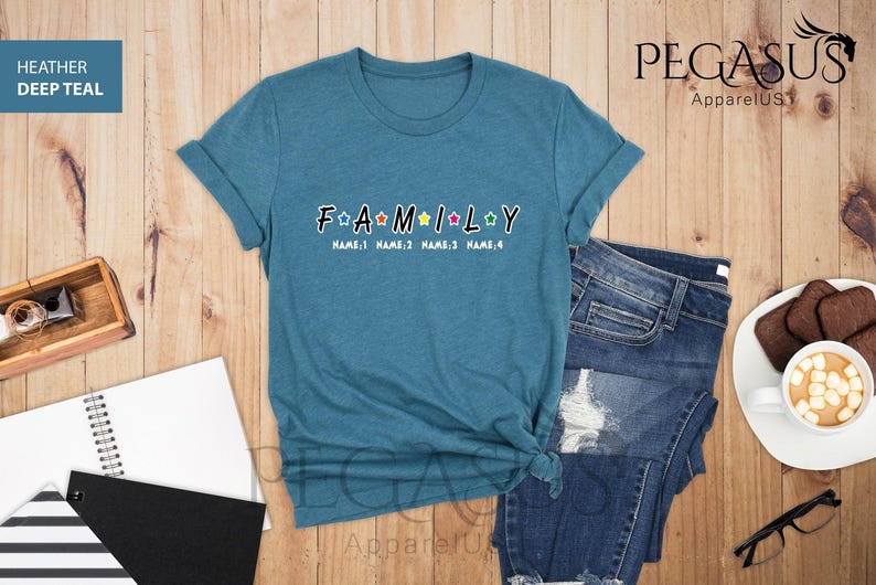 May include: A teal blue t-shirt with the word "FAMILY" in white letters with colorful stars. The text "NAME:1 NAME:2 NAME:3 NAME:4" is below the word "FAMILY".