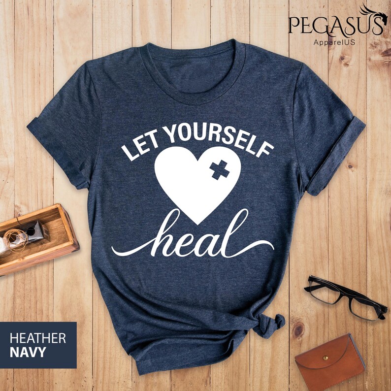 May include: A navy blue t-shirt with the text "Let Yourself Heal" in white. A white heart with a white plus sign is above the text.